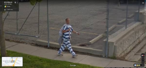 A man in a blue and white striped prison uniform walking down a public sidewalk.