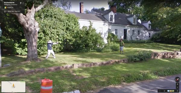 Two people in a front yard aiming bows and arrows at each other.
