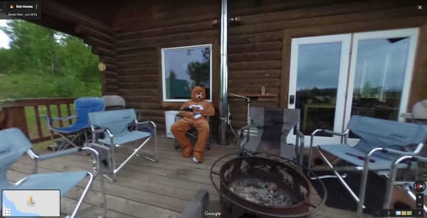 A person dressed in a full teddy bear costume sitting on a wooden deck.