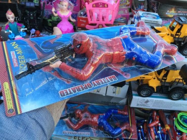 Spiderman action figure bizarrely holding a sniper rifle on a retail shelf. A hilarious funny knock off product.