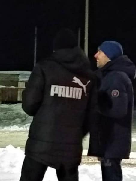 Man wearing a black winter jacket featuring the classic leaping cat logo but spelling Paum instead of Puma.
