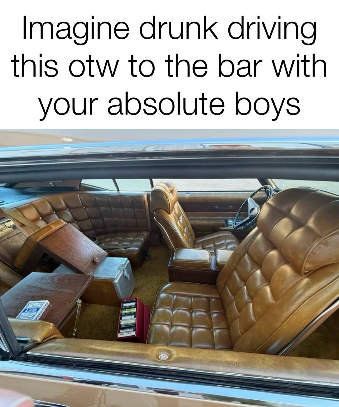 Interior of a vintage car with luxury tufted brown leather seating and a built-in wooden bar console.