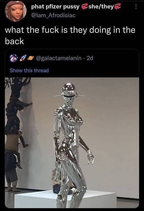 Confusing image of a chrome female robot statue with people climbing a wall in the background.