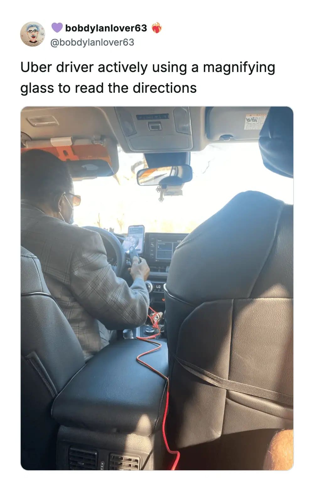 Passenger's view of an Uber driver using a magnifying glass to read a phone screen's directions.