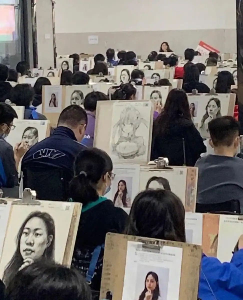 Room full of art students drawing a portrait except for one student drawing an anime character.
