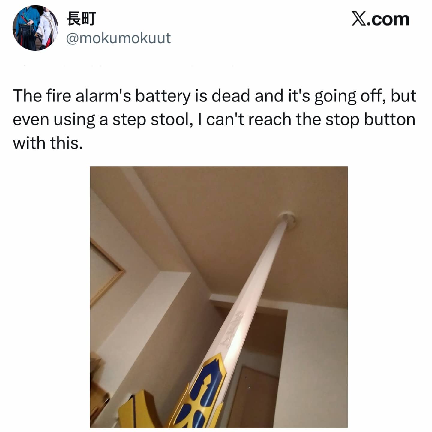 Person using a decorative anime sword to reach a chirping fire alarm on a high ceiling.