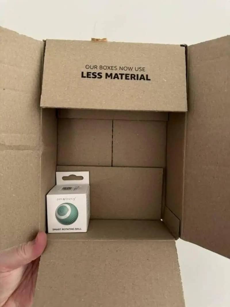Large shipping box with text claiming less material used despite containing a tiny white product box.