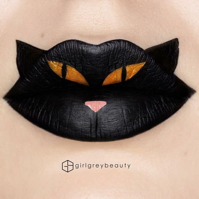 A fierce and amazing lip art design transforming the lips into a striking black cat with glowing golden slit eyes and a tiny pink nose, showcasing the precision of Andrea Reed lip art.