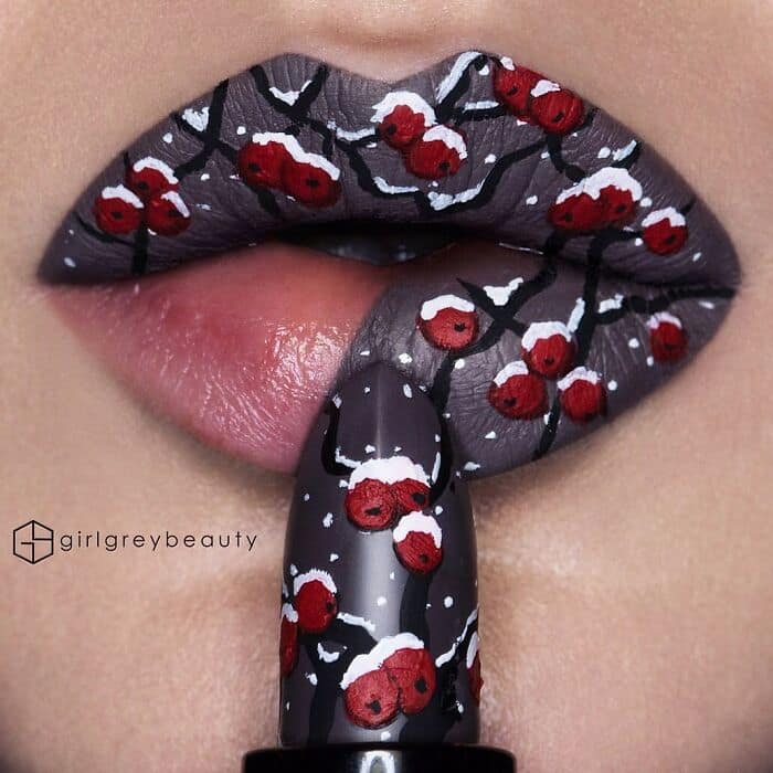A frosty, elegant winter scene created with amazing lip art, showing snow-capped branches and bright red berries flowing seamlessly from the lips onto the lipstick bullet, a classic Andrea Reed lip art composition.