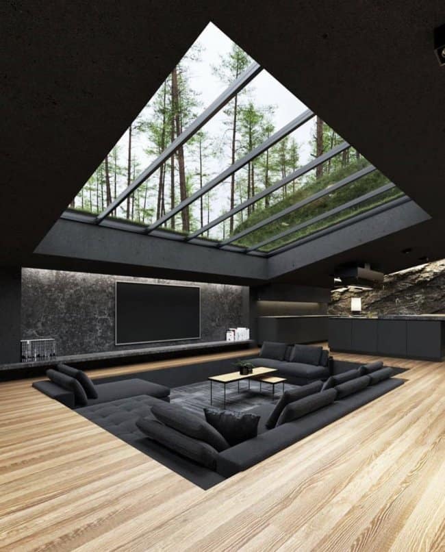 A breathtaking masculine home decor sunken living room design with dark charcoal sofas positioned directly beneath a massive skylight looking up into a pine forest.