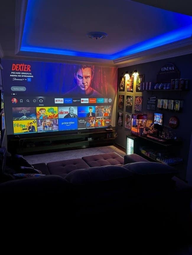 A dedicated masculine home decor movie room equipped with a wall-sized projector screen, a popcorn machine, movie posters, and cool blue LED cove lighting.
