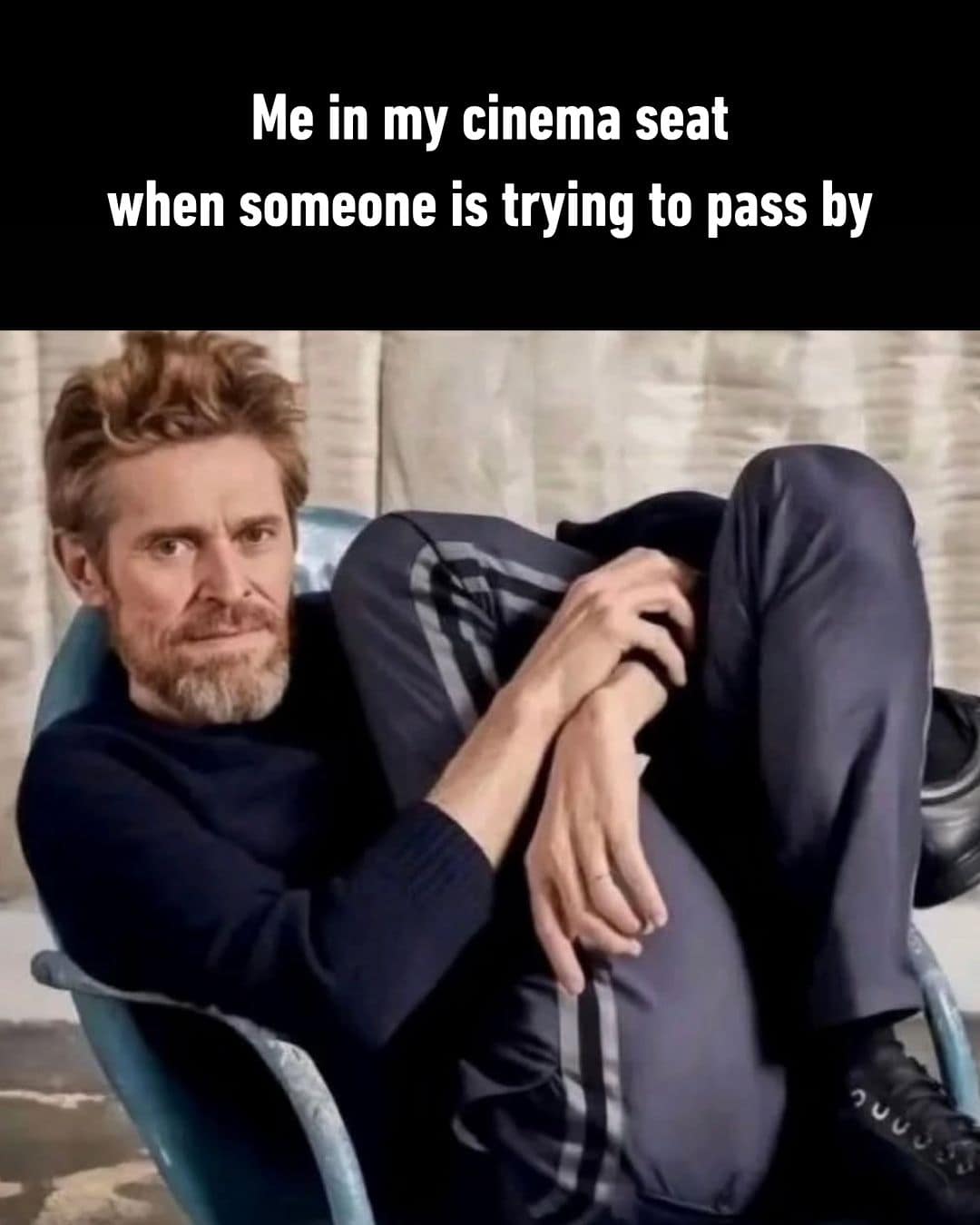 A hilarious meme featuring Willem Dafoe contorting his legs in a chair to represent the awkward physical struggle of letting someone pass by your seat in a movie theater.