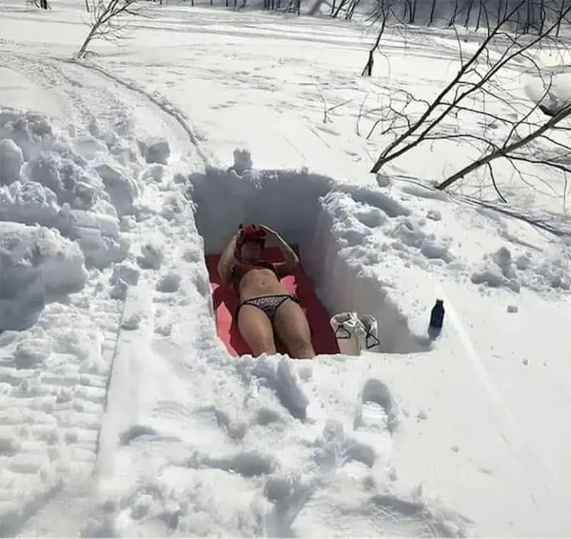A hilarious meme showing a person determined to sunbathe in a bikini despite being in a hole dug out of several feet of winter snow.