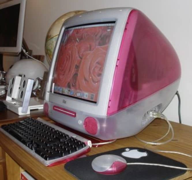 Bright pink translucent iMac G3 on a wooden desk with a matching round mouse.