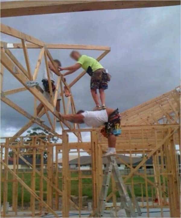 A creative osha meme solution where one construction worker acts as a human step-stool so his coworker can reach the top of the roof truss.