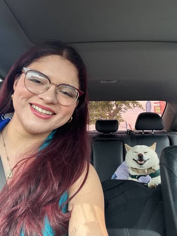 A smiling woman with reddish hair and a white Shiba Inu dog making the same expression.