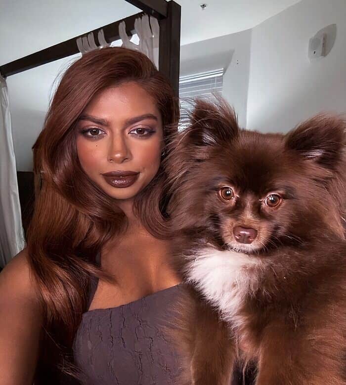 Woman with auburn hair and dark lipstick side-by-side with a fluffy brown pomeranian dog.