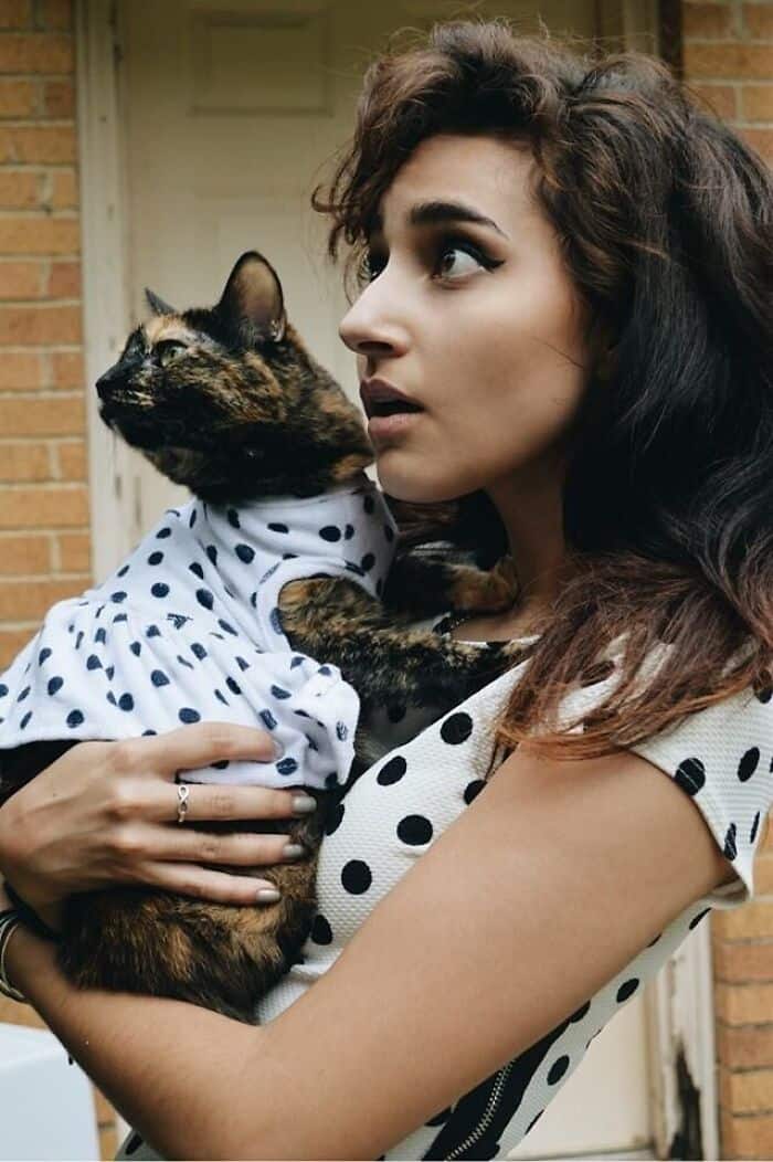 Woman in a polka-dot dress holding a tortoiseshell cat wearing a matching miniature polka-dot outfit.