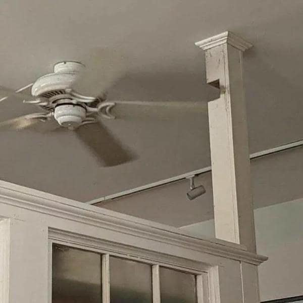 A redneck ingenuity fix where a notch has been cut out of a wooden pillar to allow the ceiling fan blade to spin through it.
