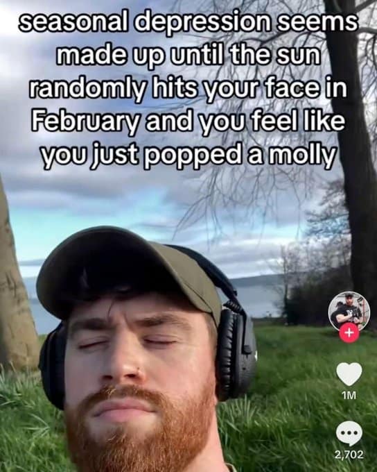 Red-bearded man with headphones closing eyes as February sun provides seasonal depression relief.