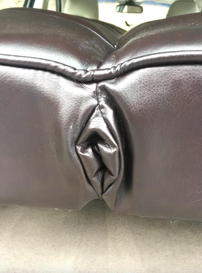 A close-up photo of brown leather car seats pressed firmly together, creating an unfortunate design where the folded upholstery forms a surprisingly detailed and accidentally nsfw crevice.