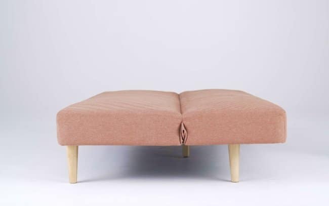 A simple pink futon bed demonstrating an unfortunate design, as the folding hinge mechanism underneath pinches the fabric in the center to create a deeply accidentally nsfw visual fold.