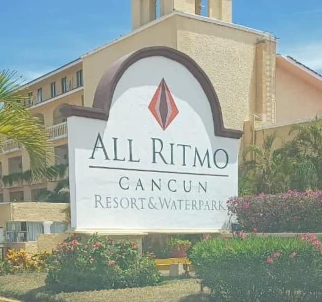 A hotel sign for "All Ritmo Cancun" featuring an unfortunate design above the text: a pink and orange vertical diamond logo that looks suspiciously and accidentally nsfw.