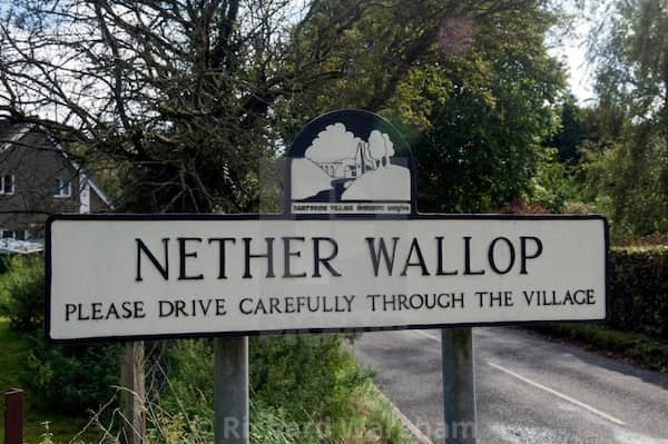 White village entry sign for Nether Wallop advising drivers to travel carefully through the area.