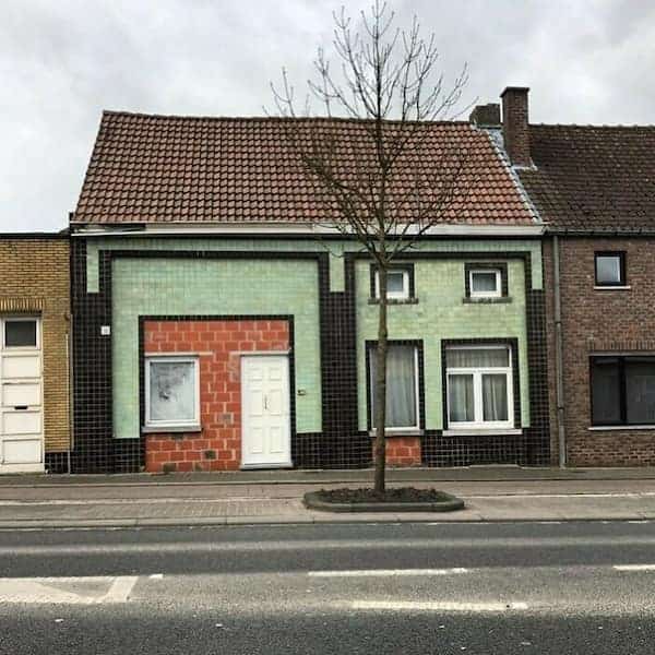 A house in Belgium with a bizarre, asymmetrical facade featuring mismatched green tiles and brick patterns.