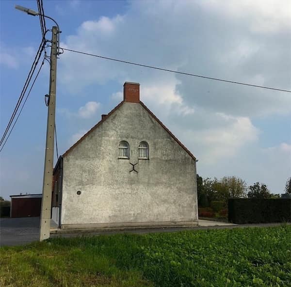 A plain Belgian house facade with two small windows and a crack that looks like a cat.