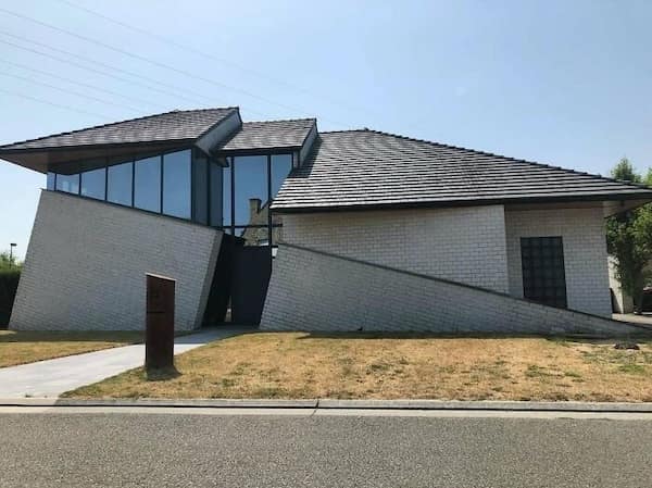 A slanted Belgian house with white brick walls and windows that appear to be sliding downward.