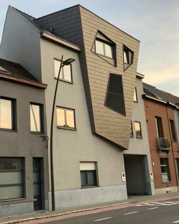 A grey Belgian building with a wood-paneled section shaped like a screaming or surprised human face.
