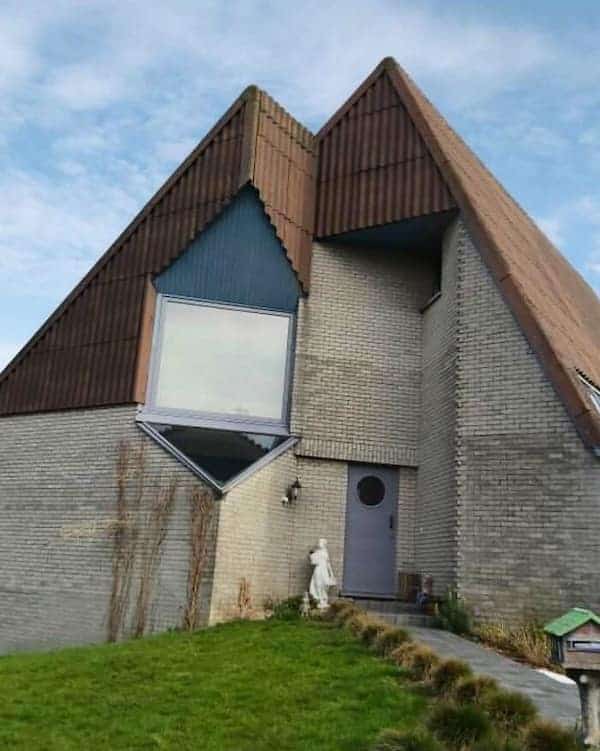 A Belgian home with a sharp, triangular roof and a single oversized window placed at an angle.