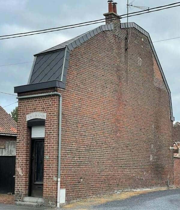 A narrow brick Belgian house that is mostly a tall, flat wall with one tiny door.