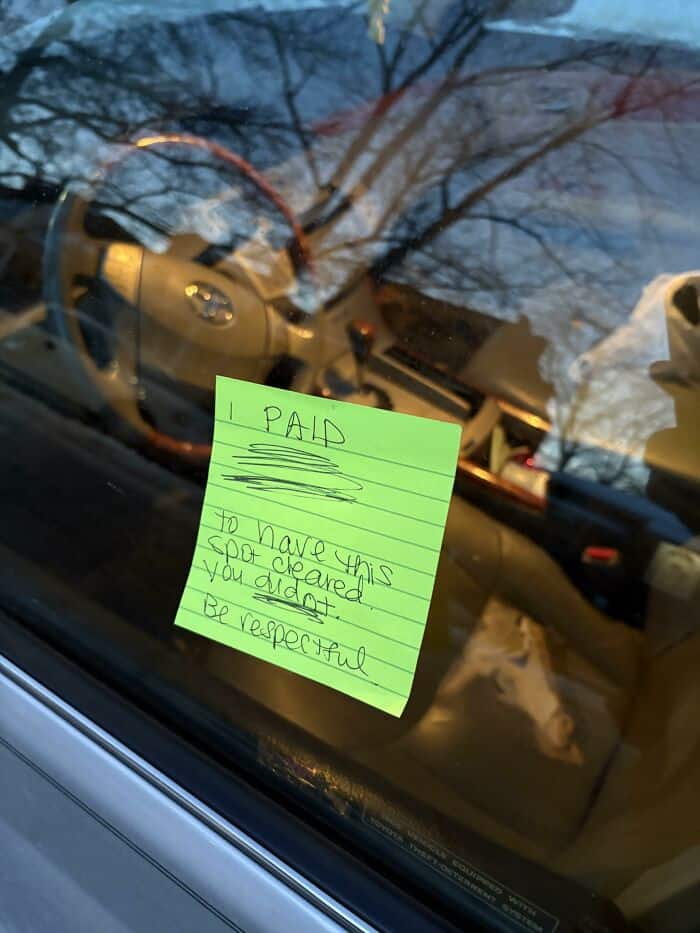 Neon green sticky note on a car window telling a driver to be respectful of spots.
