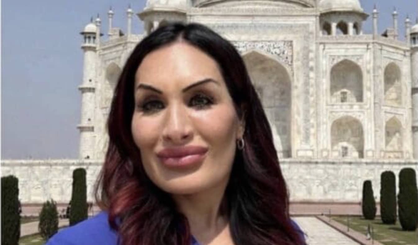 Woman with dark hair and blue top posing for a selfie at the Taj Mahal.