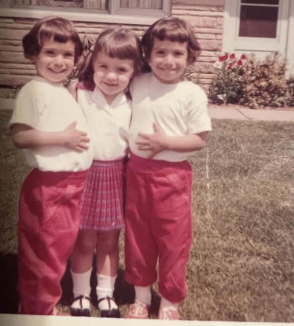 vintage outdoor photo of three young girls showcasing classic 80s haircuts. The twins on the ends sport short, rounded bobs with thick, straight-across bangs, while the girl in the middle wears her hair in pigtails with matching blunt fringe.