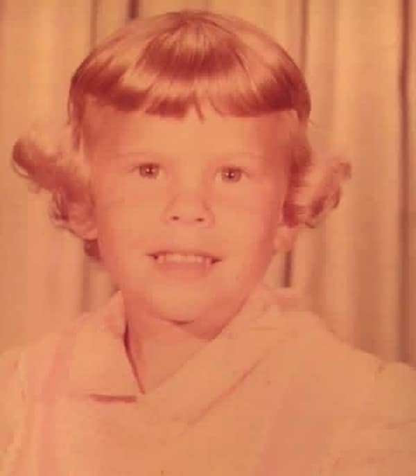 sepia-toned photo of a young girl showcasing a playful 80s haircut. Her hair is styled into short, flared-out "wings" at the sides with thick, curled-under bangs, a look that defines the early part of the decade.