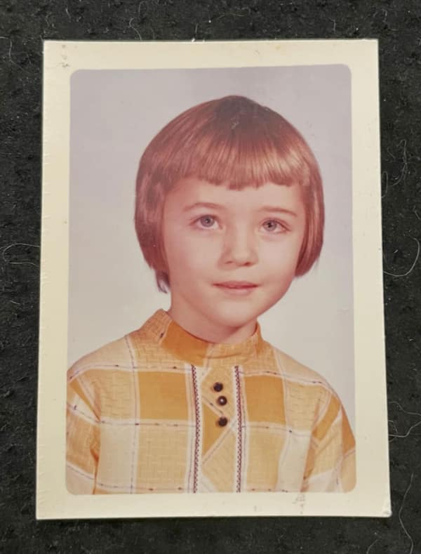 A professional school portrait of a young girl with a sleek 80s haircut bowl cut. The reddish-brown hair is cut in a precise, rounded line that frames her face, paired with short, blunt-cut bangs.