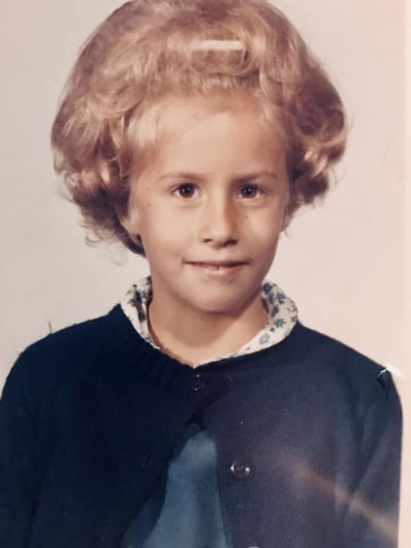 A young girl with a massive, gravity-defying 80s haircut. The style is a giant, rounded "pouf" of teased and hairsprayed blonde curls, embodying the "bigger is better" hair philosophy of the decade.
