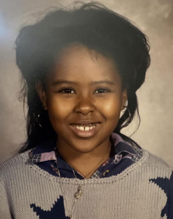 A young girl’s school portrait showing a voluminous, dark 80s haircut. This "shag" style includes a mountain of teased hair on top and at the sides, tapering down into longer, thinner layers in the back—a precursor to the classic mullet.