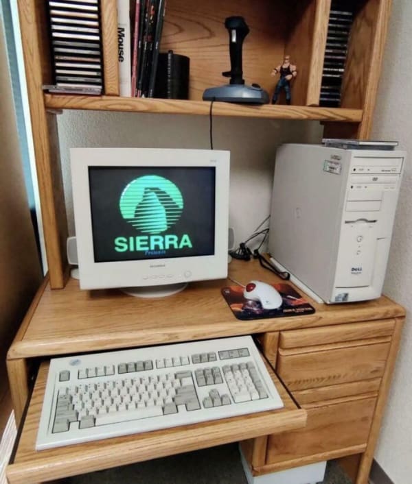 A highly accurate 90s meme showcasing the ultimate retro computer desk setup, complete with a chunky keyboard tray, a joystick, and a heavy CRT monitor displaying the Sierra games logo for maximum 90s nostalgia.