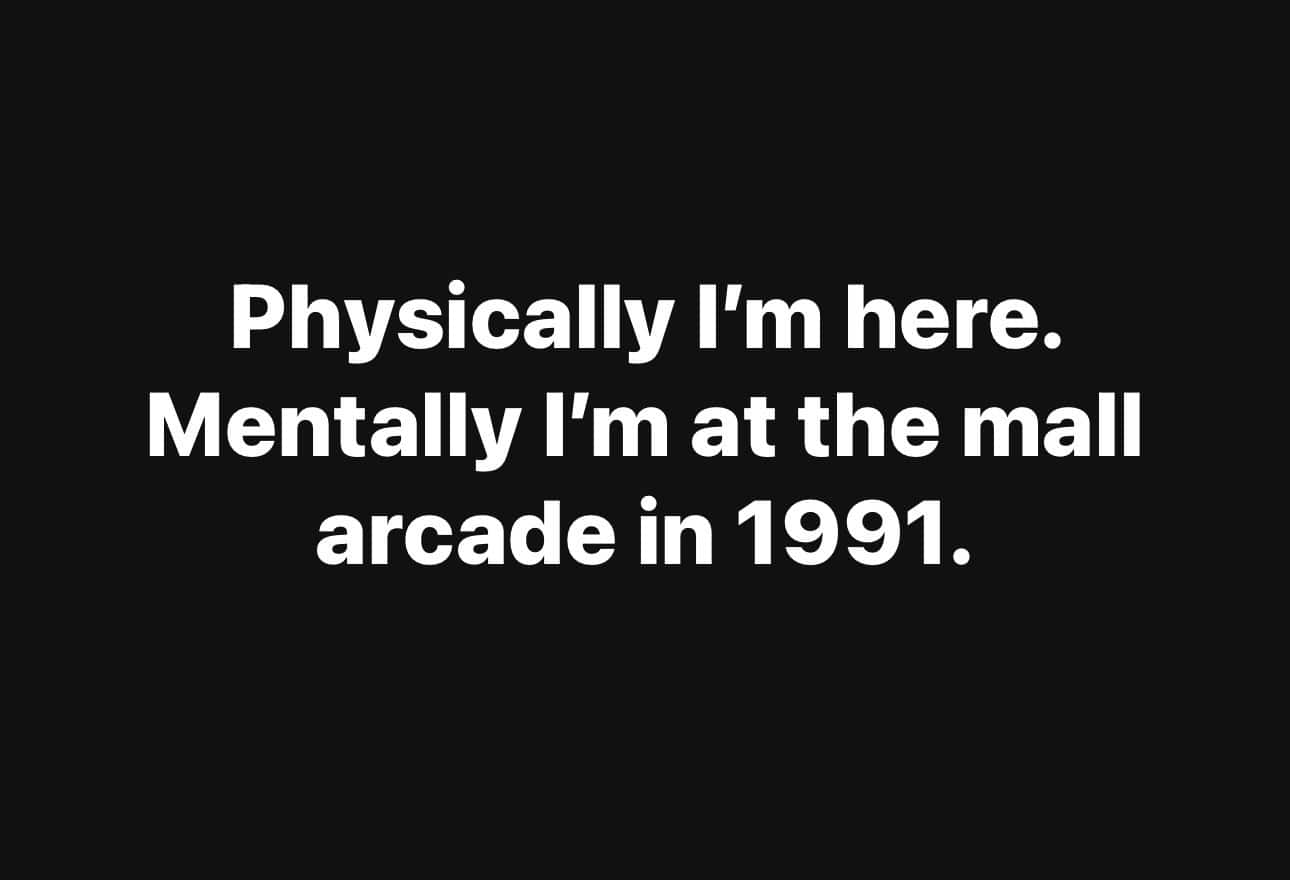 text-only nostalgia meme on a black background that captures a mood: "Physically I'm here. Mentally I'm at the mall arcade in 1991."