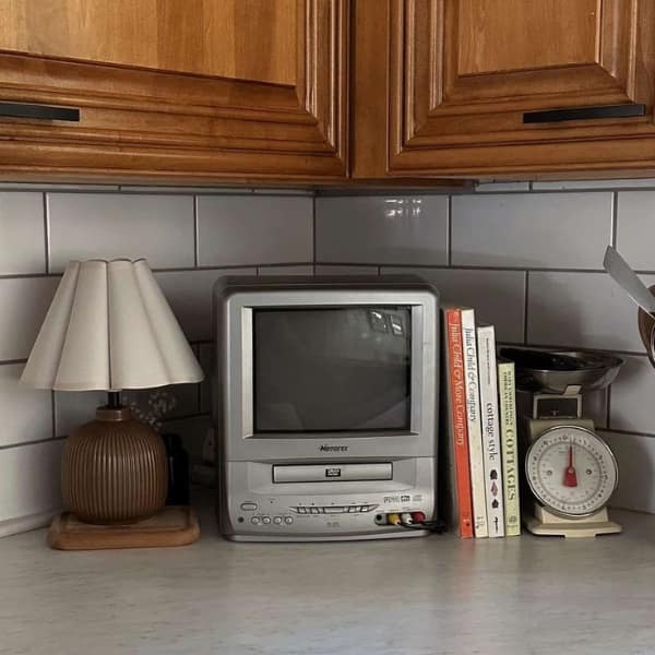 A deeply aesthetic 90s meme showing a chunky silver Memorex tube TV with a built-in DVD and VCR player resting perfectly on a kitchen counter, delivering a massive wave of cozy domestic 90s nostalgia.