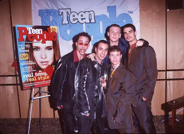 classic boy band moment in 90s pictures featuring the Backstreet Boys posing together in shiny, oversized suits in front of a promotional banner for Teen People magazine.