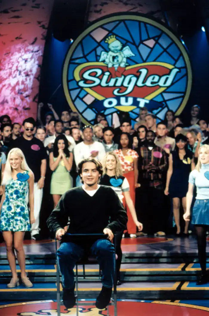 classic television screenshot in this collection of 90s pictures showing the set of MTV's Singled Out, featuring a young contestant sitting nervously in a chair while surrounded by cheering participants.