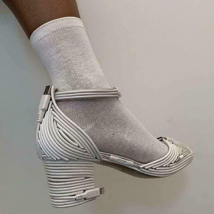 A person wearing a high heel platform shoe constructed entirely out of tightly wrapped white USB charging cables. A bizarre fashion diy fail.