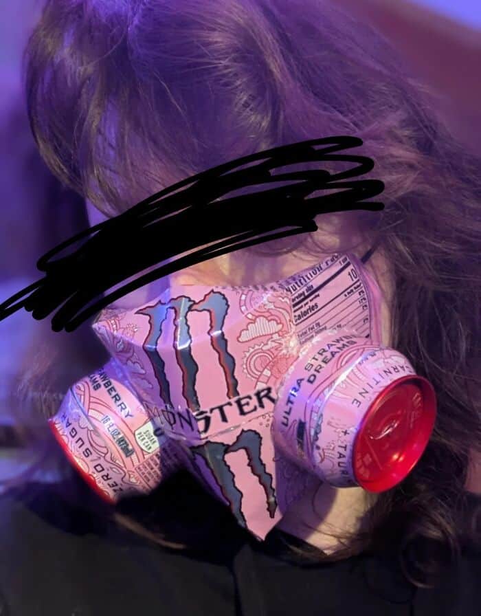 A person wearing a functional-looking cyberpunk gas mask crafted entirely out of cut up pink Monster Energy drink cans. A wildly creative but hilariously bad DIY project.