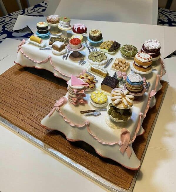 A masterpiece cake designed to look like a banquet table covered in miniature individual cakes.