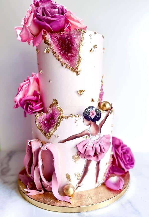 An elegant two-tier pink ballet cake featuring edible geode crystals, gold leaf, and a ballerina.